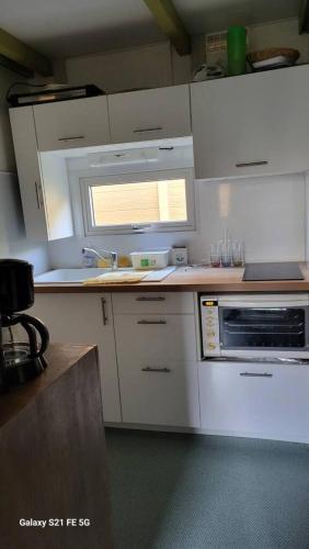 une cuisine avec des armoires blanches, un évier et une fenêtre dans l'établissement Chalet climatisé avec patio en Haute Corse 5 couchages, à Camp du Cap Sud