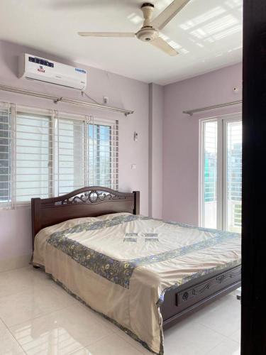 um quarto com uma cama, uma ventoinha de tecto e janelas em 4 Beds Condo Holiday Home at Bashundhara Dhaka em Daca