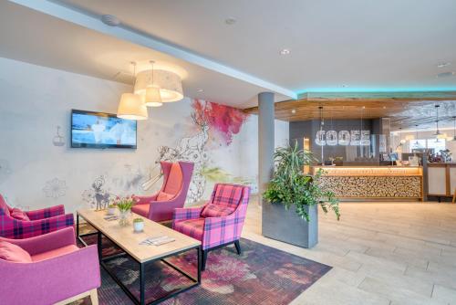 a lobby with pink chairs and a table and a counter at COOEE alpin Hotel Bad Kleinkirchheim in Bad Kleinkirchheim