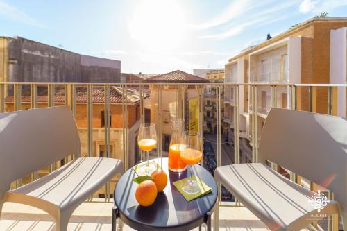 a table with two glasses of wine and oranges on a balcony at Matteotti Luxury Residence in Siracusa