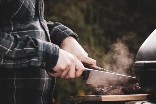 a person holding a knife over a grill at Pimishka Chalet-Cottage-Studios in Bouchette