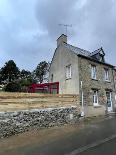a stone house with a red window and a stone wall at Le Marlo in Poilley