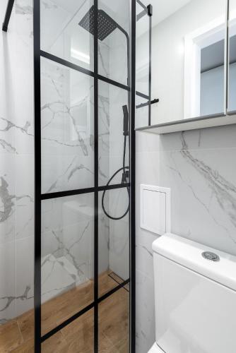 a bathroom with a glass shower door next to a toilet at Kairos Apartments - Amber - darmowy Parking, ścisłe centrum in Gliwice