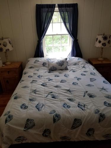 a bed with a blue and white comforter and a window at Scallop's Nest in Dennis Port