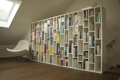 a wall of books in a room with a white chair at La Ferme de la Praz - Rooms with a View in La Praz