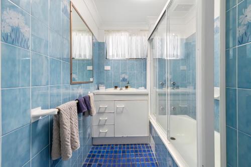 uma casa de banho em azulejos azuis com um lavatório e um chuveiro em Dolphin View on South Esplanade em Bongaree