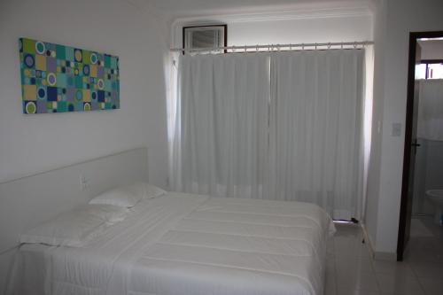 a white bedroom with a white bed and a window at Paraiso Moradas in Porto Seguro
