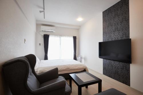 a bedroom with a bed and a chair and a television at New Normal Hotel in NAGO ニューノーマルホテルイン名護 in Nago