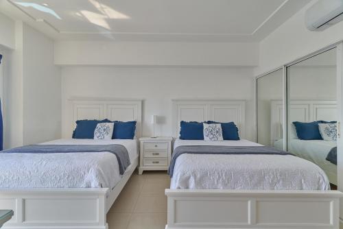two beds in a white room with blue pillows at Sunset View 2BR Apartamento Juan Dolio Las Velas in Juan Dolio