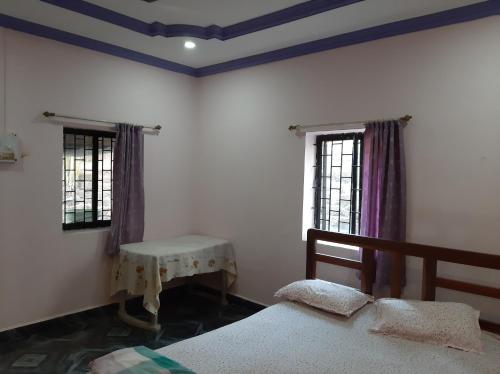 a bedroom with two beds and a table and two windows at Dias guest house in Canacona