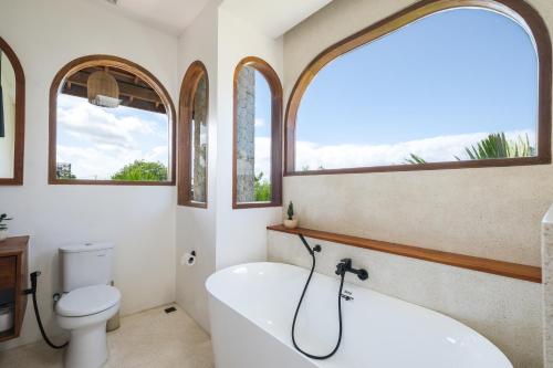 a bathroom with a tub and a toilet and two windows at The Arki Villa in Canggu