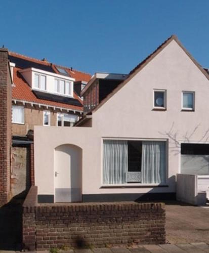 a white house with a brick wall at Have a nice stay! - Zomerhuis Toda Cambia dicht bij strand in Noordwijk aan Zee