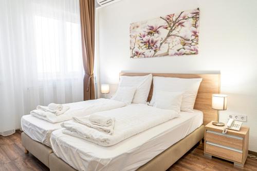 a bedroom with a bed with white sheets and a painting at Ózoon Hotel in Nyíregyháza