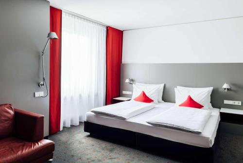 a bedroom with a bed with red pillows and a chair at Vienna House Easy by Wyndham Stuttgart in Stuttgart