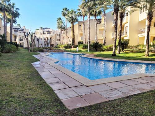 una piscina con palmeras y edificios en El Oasis de las Palmeras @ Roda Golf & Beach resort, en San Javier