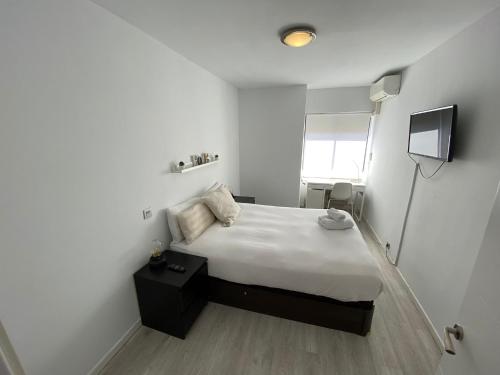a small white bedroom with a bed and a television at Apartamento Cuzco in Madrid