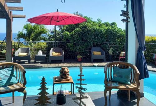 een zwembad met 2 stoelen en een rode parasol bij Suite INDIGO JACUZZI PRIVE PISCINE VUE MER acces cuisine laverie in Saint-Pierre