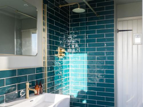 a blue tiled bathroom with a sink and a mirror at Stag Cottage in Penrith