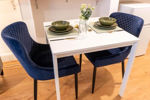 Flat 02 Studio Luton 53 free Parking في لوتون: طاولة بيضاء مع الكراسي الزرقاء والأطباق والزهور