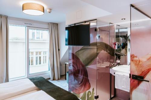 ART-INN Design Self-Check-in-Hotel في لينز: غرفة نوم بسرير وتلفزيون على جدار زجاجي