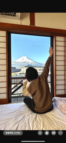 a woman sitting on a bed looking out a window at Guest house En in Fujiyoshida