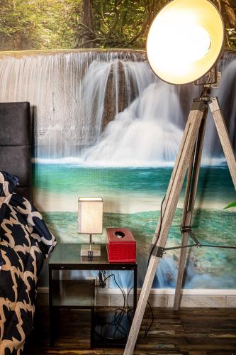 Cette chambre comprend une table avec une lampe et une fresque murale représentant une cascade. dans l'établissement ArtistMemory Appartement, à Corbeil-Essonnes