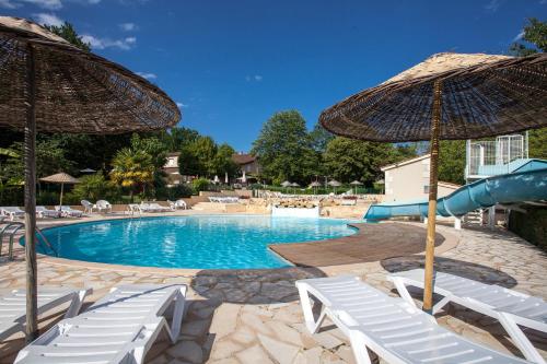une piscine avec des chaises blanches et des parasols dans l'établissement Camping le Clou, à Coux-et-Bigaroque