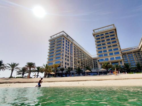 a person standing in the water on a beach with two buildings at Luxurious 2 bedroom Beachfront Apartment - direct seaview in Ras al Khaimah