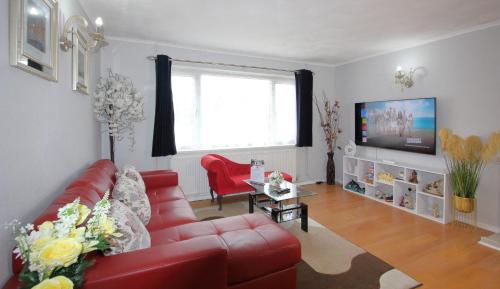 a living room with a red couch and a tv at Cheerful 3 Bedroom 2 Bathroom Bungalow by CozyNest in Earley