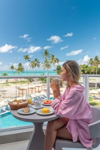 una mujer sentada en una mesa con comida en un balcón en Maragogi Brisa Exclusive Hotel, en Maragogi
