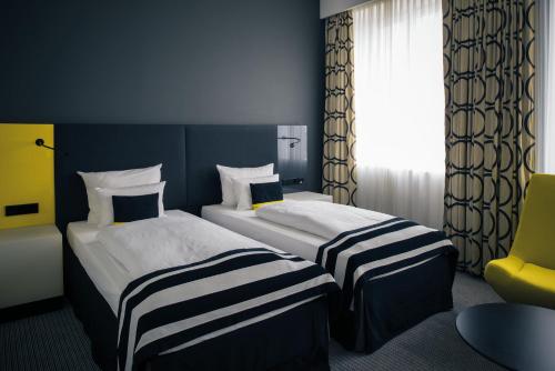 a hotel room with two beds and a yellow chair at Vienna House by Wyndham Andel's Berlin in Berlin