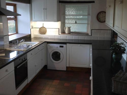 cocina con armarios blancos, lavadora y secadora en Tranquil 3-Bed Cottage Near Lake Vyrnwy, en Hirnant