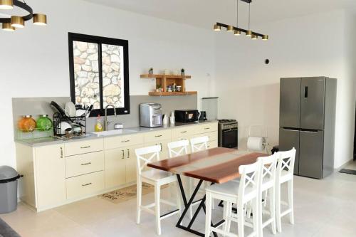 a kitchen with a wooden table and a refrigerator at ממלכת החלומות - וילה מושלמת עם ממ"ד בריכה פרטית ונוף גליל in ‘Ein el Asad