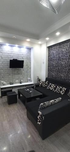sala de estar con sofá negro y TV en Apartments Lezzet, en Tiflis