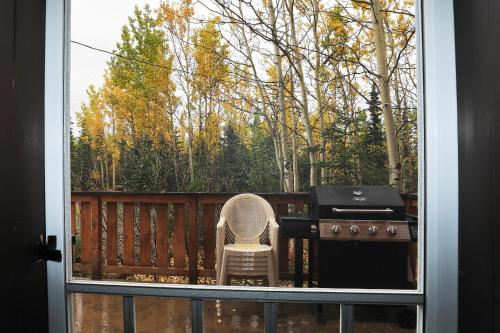 a patio with a grill and a chair outside a window at Denali Park View Family Log Cabin in McKinley Park