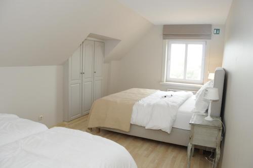 a white bedroom with two beds and a window at Vakantiewoning La Cereza in Opbrakel