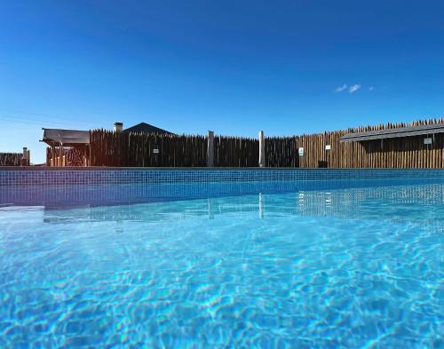 a swimming pool with blue water in front of a fence at Kuanza Farmhouse and Lodge in Zambujeira do Mar