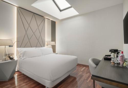 a white bedroom with a white bed and a desk at NH Collection Salamanca Palacio de Castellanos in Salamanca