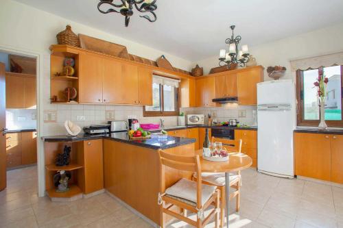 a kitchen with wooden cabinets and a table and a refrigerator at Villa Styliani in Argaka