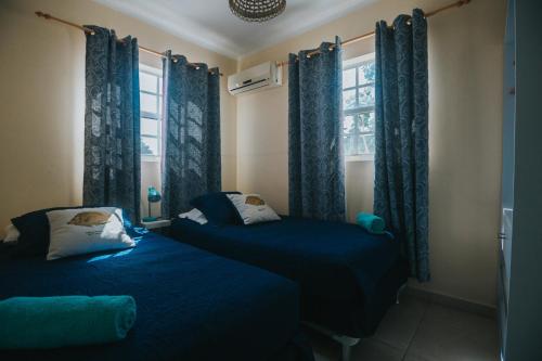 two beds in a room with blue curtains and a window at Dushi Villa in Palm-Eagle Beach