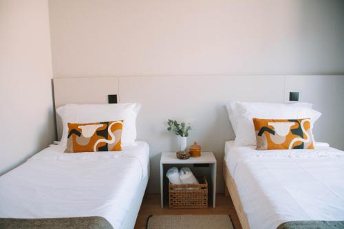 two beds with white sheets and orange pillows in a room at Just Like Home - Moledo Slow Living in Moledo