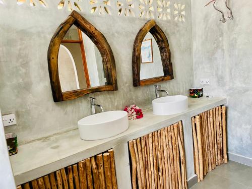 a bathroom with two sinks and two mirrors at Blue Reef Sport & Fishing Lodge and Bungalows in Jambiani