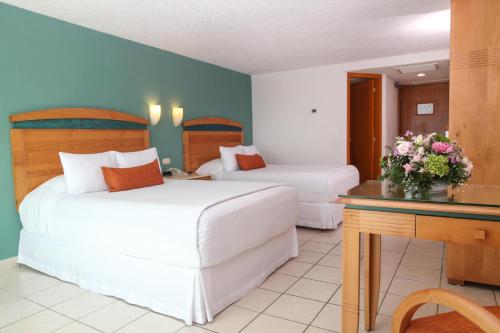 a hotel room with two beds and a desk with flowers at Casa Mexicana Cozumel in Cozumel