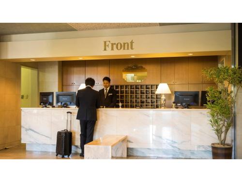 due uomini in piedi al bancone di un hotel di Hotel Areaone Hiroshima Wing - Vacation STAY 62250v a Higashihiroshima