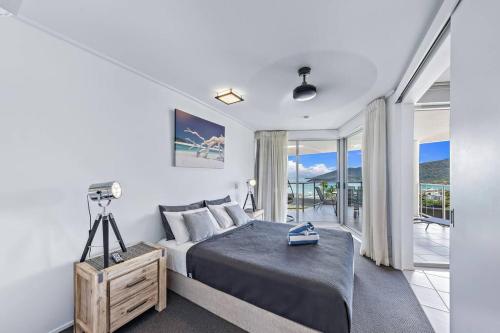 a white bedroom with a bed and a balcony at Whitsunday Wonderview in Airlie Beach