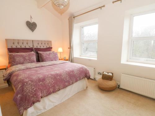 a bedroom with a purple bed and two windows at Springwood Cottage in Holmfirth