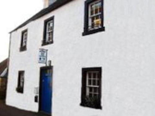 a white building with black windows and a blue door at Cosy cottage flat in Inveraray