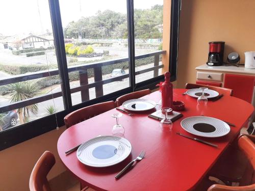 une table rouge avec des chaises et une table rouge avec des assiettes dans l'établissement Appartement 4 couchages à Capbreton avec piscine, tennis et plage à pied - FR-1-239-867, à Capbreton