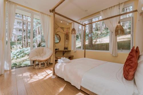 a bedroom with a bed and a chair and windows at Dahlia Dalat in Xuan An