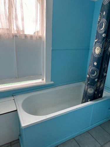 een bad in een blauwe badkamer met een raam bij Club Hotel Pahiatua in Pahiatua
